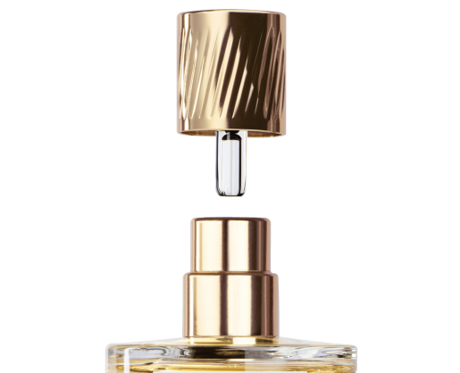 A close-up of a perfume bottle with a gold cap suspended above the bottle and short fragrance applicator named Note. A transparent diptube tube is also visible and inside the bottle is light yellow liquid indiciative of fragrance.