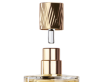 A close-up of a perfume bottle with a gold cap suspended above the bottle and short fragrance applicator named Note. A transparent diptube tube is also visible and inside the bottle is light yellow liquid indiciative of fragrance.