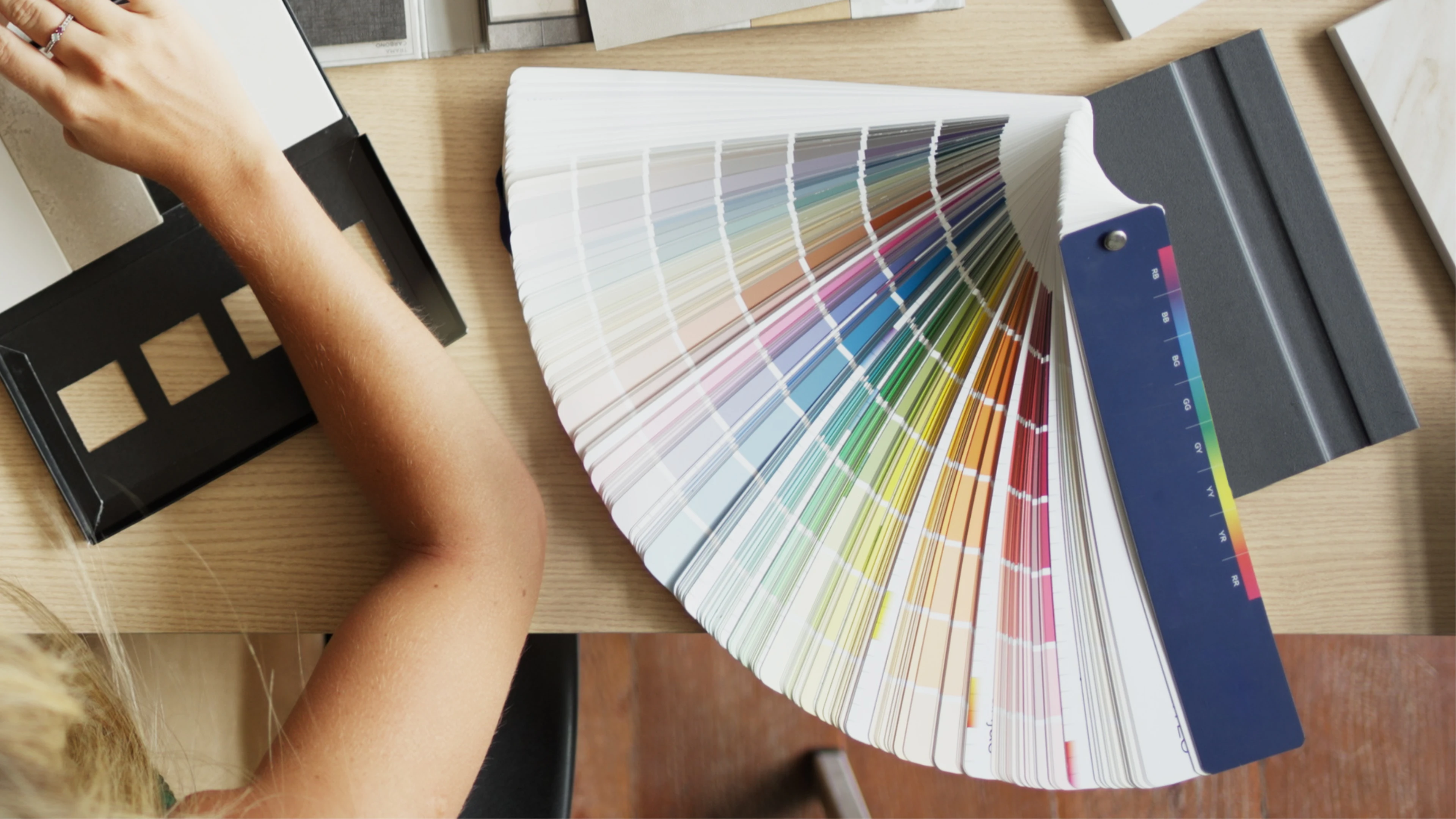 A top view of a person sitting at a desk with a book of color swatches next to them.