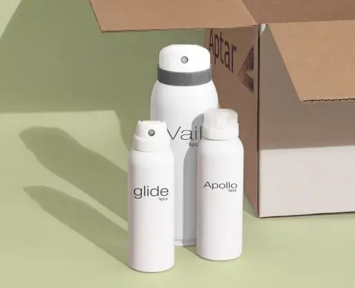 Three white aerosol bottles beside an open cardboard box on a green background, showing product packaging.