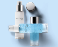 Three transparent airless glass dispensers labeled ASTREA are displayed. Two bottles are positioned vertically,one with a silver actuator exposed, and the other with its silver cap in place. The third bottle lies horizontally in the foreground, featuring a white actuator paired with a clear cap.