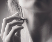 A person uses a fragrance applicator labeled Note to apply perfume to their neck. The black and white image captures a close-up of the neck and hand, highlighting the elegance of this intimate moment.