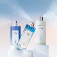 Three elegant bottles of body spray labeled INUNE and AQUA SILK are displayed on white pedestals, with two bottles high definition spray fragrance misting against a soft blue and pink gradient background.