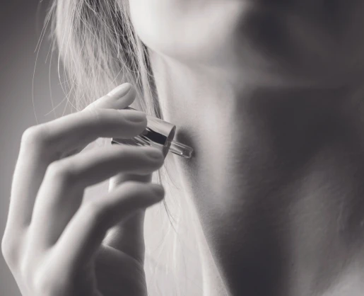 A person uses a fragrance applicator labeled Note to apply perfume to their neck. The black and white image captures a close-up of the neck and hand, highlighting the elegance of this intimate moment.