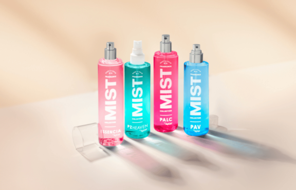 Four colorful mist spray bottles labeled MIST stand upright on a light surface with a soft, blurred background. Featuring a customizable spray pump labeled PAV, the pink, turquoise, and blue bottles display different product names.