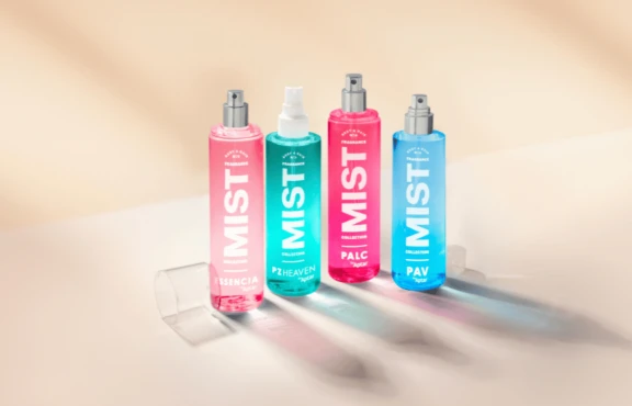 Four colorful mist spray bottles labeled MIST stand upright on a light surface with a soft, blurred background. Featuring a customizable spray pump labeled PAV, the pink, turquoise, and blue bottles display different product names.