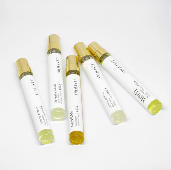 Five STILO glass perfume sample vials with gold caps are arranged diagonally on a white surface. Each vial features Aptar's refillable fragrance mini packaging, designed for on-the-go scent.