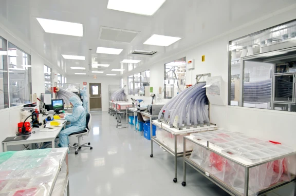 Two technical workers wearing full blue gowning with head covering working in nasal device manufacturing and inspection.