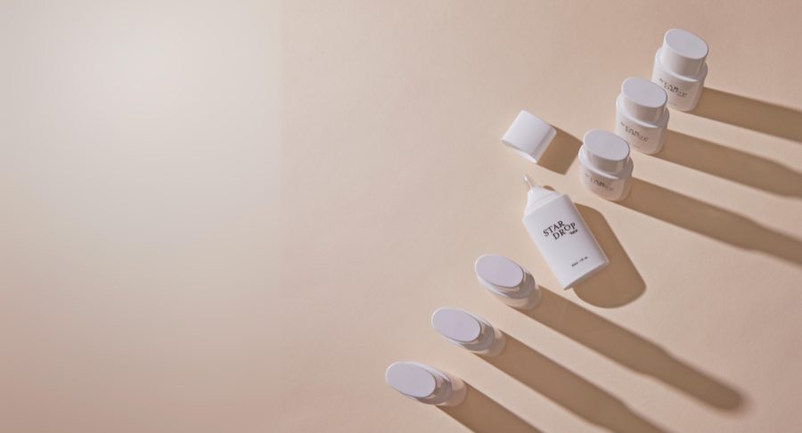 A group of Star Drop, drop-by-drop dispensing solution , are arranged diagonally on a beige surface, casting long shadows to the right. The left side of the image fades into a soft, empty background.