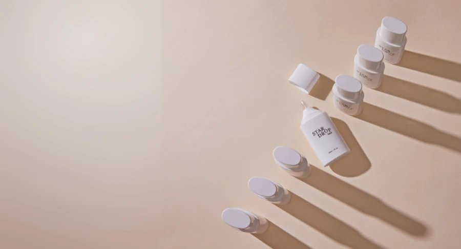 A group of Star Drop, drop-by-drop dispensing solution , are arranged diagonally on a beige surface, casting long shadows to the right. The left side of the image fades into a soft, empty background.