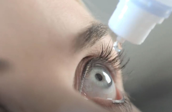 A close-up of a female with light blue eyes receiving an eye drop from Aptar Pharma’s ophthalmic squeeze dispenser. The drop is about to be dispensed near her upper eyelashes, showing the precision of the eye care dropper.