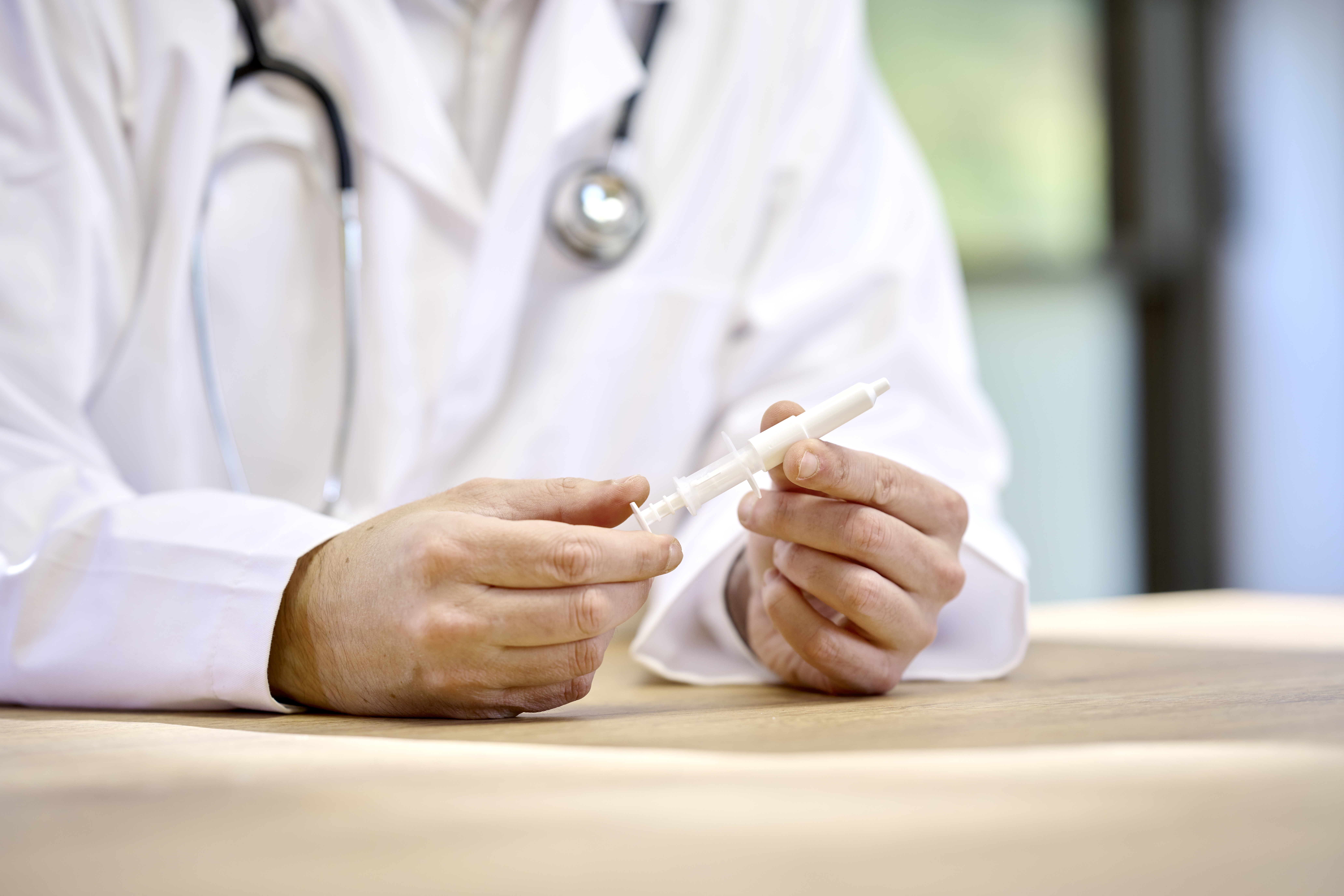 Physician in a lab coat holding Aptar Pharma white nasal liquid device in his hands while seated at a desk for vaccination.