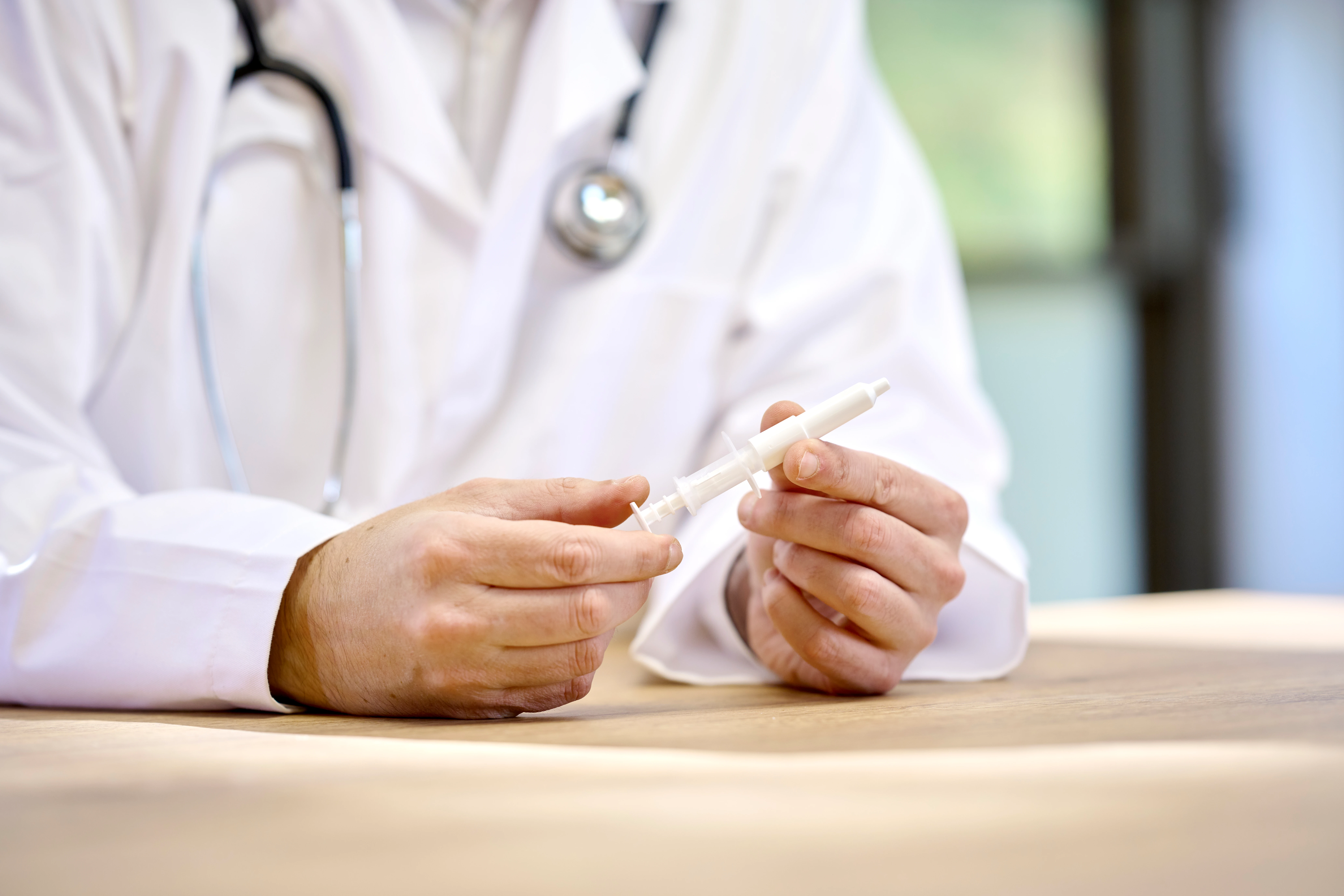 Physician in a lab coat holding Aptar Pharma white nasal liquid device in his hands while seated at a desk for vaccination.