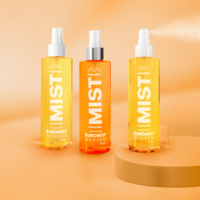 Three spray bottles labeled EUROMIST HEAVEN stand on a peach-colored surface and background, with one bottle with a silver collar ,and one spraying a fine mist. The bottles are in shades of yellow and orange.