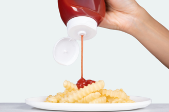 Ketchup being squeezed onto french fries on a white plate