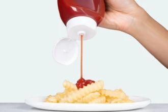 Ketchup being squeezed onto french fries on a white plate