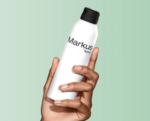A hand holds a white spray can with a black premium twist to lock aerosol actuator against a light green background. The can is labeled Markus by Aptar.