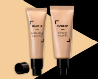 Two beige makeup tubes, designed as airless pump tubes for skincare and cosmetic formulas, stand upright on a black and beige geometric background. One tube has its black cap off and lying beside it.