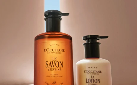 A Loccitane Hand Soap and Smaller Hand Lotion with Shiny Black Custom Dispensing Pumps Stand on a Gray Beige Background with a Opening on the Sky
