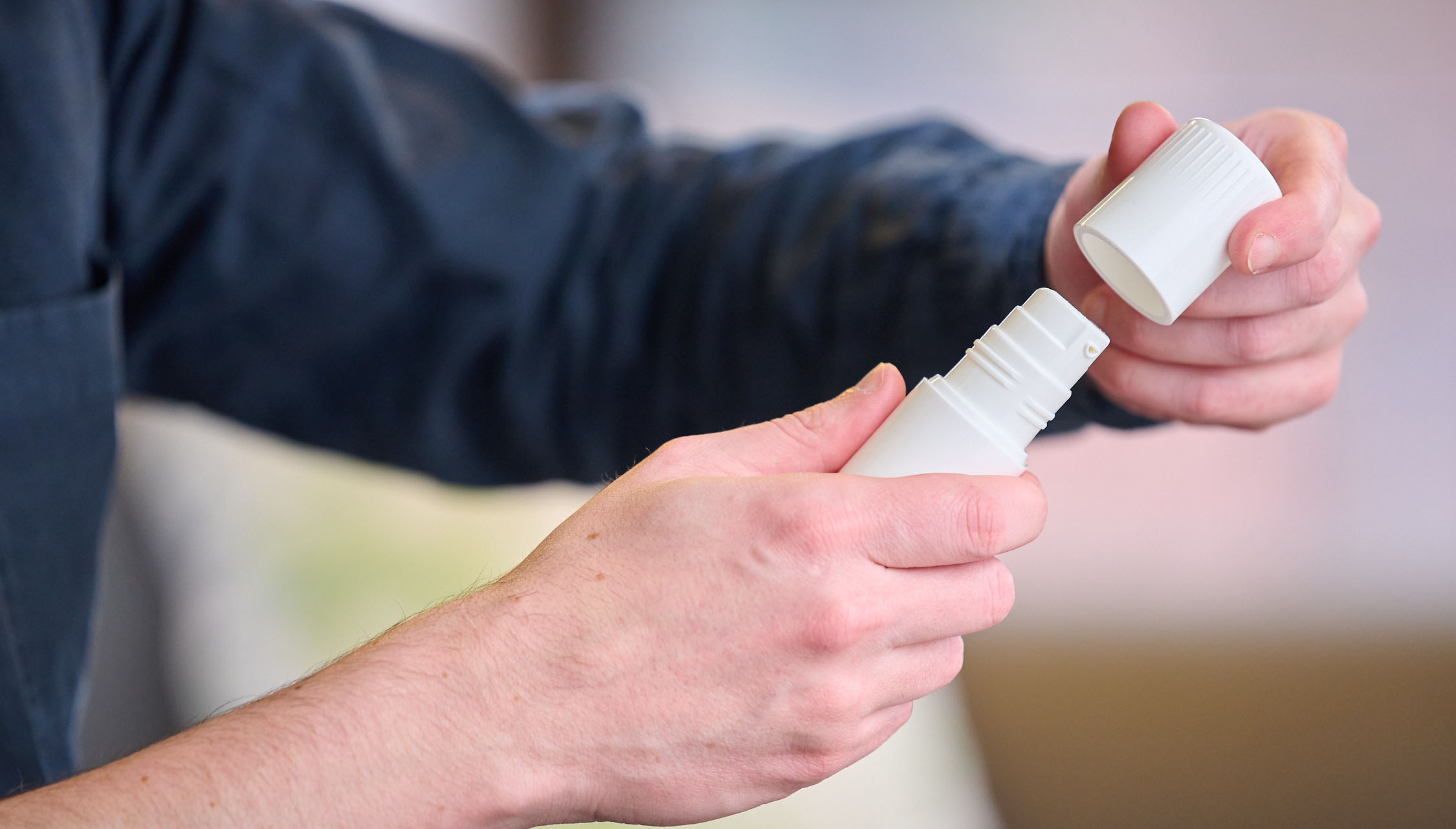 Man in blue collared shirt opens child resistant cover to Aptar Pharma Airless+ dermal drug delivery device with both hands