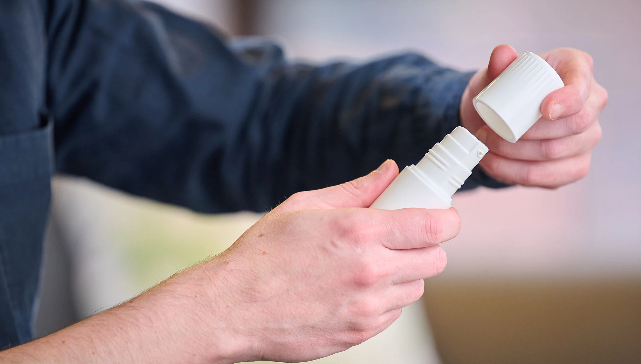 Man in blue collared shirt opens child resistant cover to Aptar Pharma Airless+ dermal drug delivery device with both hands
