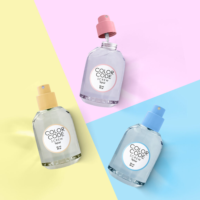 Three perfume bottles labeled COLOR CODE SCREW by Aptar, 50 ml, 80 µl, each with a refillable plastic fragrance pump and vibrant spray caps in pink, yellow, and blue, are arranged on pastel yellow, pink, and blue backgrounds.