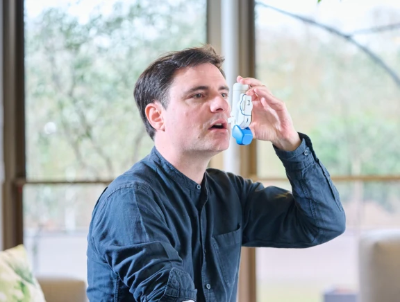 White and blue BAI inhaler device used to administer drug product by man in blue shirt with dark hair.