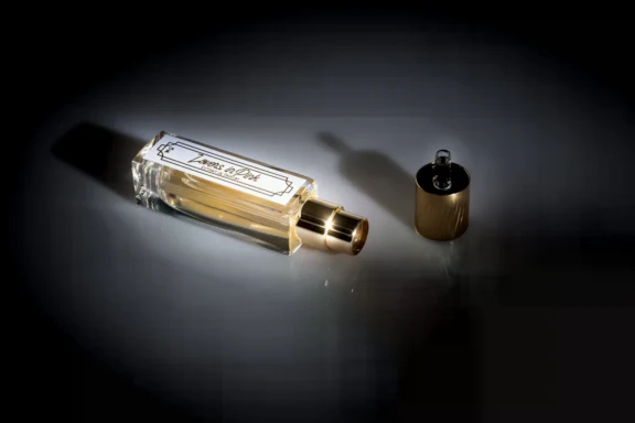 A rectangular glass perfume bottle, designed with a fragrance applicator for oil, with a gold cap lying beside it on a dark, spotlighted surface.