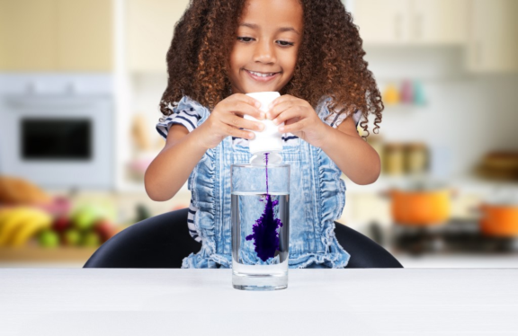 Little girl squeezing mio into a glass of water