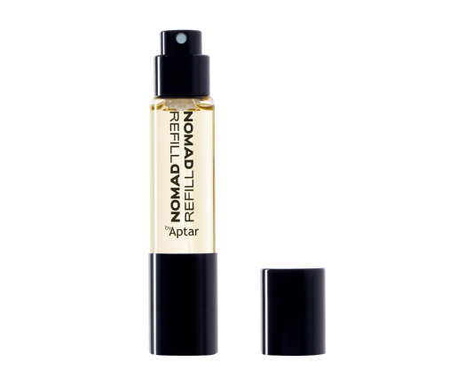 A small, clear glass bottle with yellow liquid that indicates fragrance, labeled NOMAD REFILL by Aptar, stands upright with its black cap beside it on a white background an example of stylish refillable mini fragrance packaging.