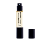 A small, clear glass bottle with yellow liquid that indicates fragrance, labeled NOMAD REFILL by Aptar, stands upright with its black cap beside it on a white background an example of stylish refillable mini fragrance packaging.
