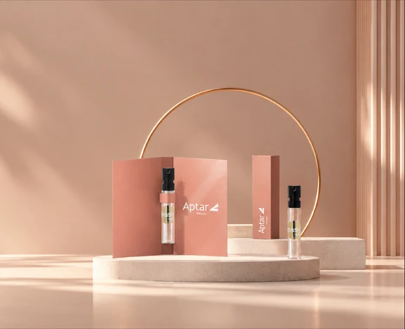 Easy Spray fragrance sampling spray vials and a branded sampling card are displayed on a tabletop with the Aptar Beauty logo, showcasing compact fragrance discovery formats.