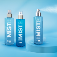 Three blue bottles labeled MIST COLLECTION PAV by Aptar are displayed on a light blue surface, indicating the product is a customizable spray pump. Two bottles are closed while one sprays mist into the air against a blue gradient background. The actuators are white.