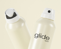 Two white aerosol cans labeled Glide by Aptar, and Apollo by Aptar are arranged on a pink background, partially inside a brown cardboard box with Aptar printed in bold black letters to highlight the design of  e-commerce capable aerosol products