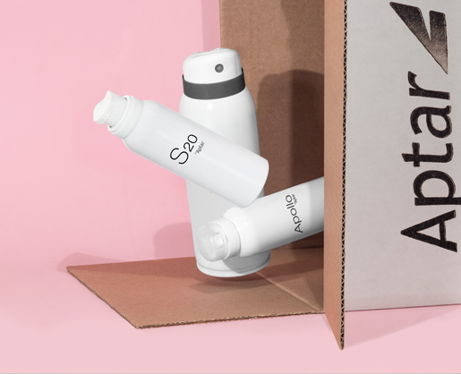 Close-up of three white spray bottles labeled S20 and Apollo, partially placed inside a brown cardboard box with 'Aptar' printed on the side. The S20 bottle features a contemporary upright aerosol actuator. 