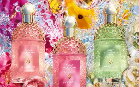 Three Peach Pink and Green Fragrance Bottles of Guerlain Aqua Allegoria Perle with Golden Caps and Details on Flower and Droplets Background
