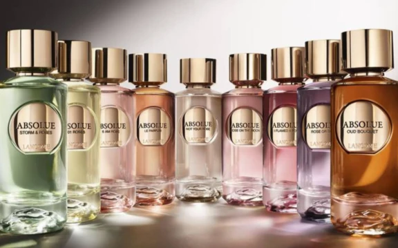 A row of colorful Absolute perfume bottles with gold caps, each featuring a different fragrance label and a HDS INUNE, ahigh definition spray fragrance pump, displayed on a reflective surface with a gradient background.