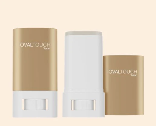 Two OvalTouch face sticks in gold and white, one without the cap, on a beige background