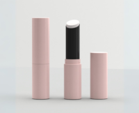 A pink lipstick-style tube with a Guided Lipstick Mechanism, cap removed to reveal a white balm stick inside. The cap stands upright beside the open tube against a plain, light-colored background, showcasing the innovative Stylist Guided Lipstick Mechanism.