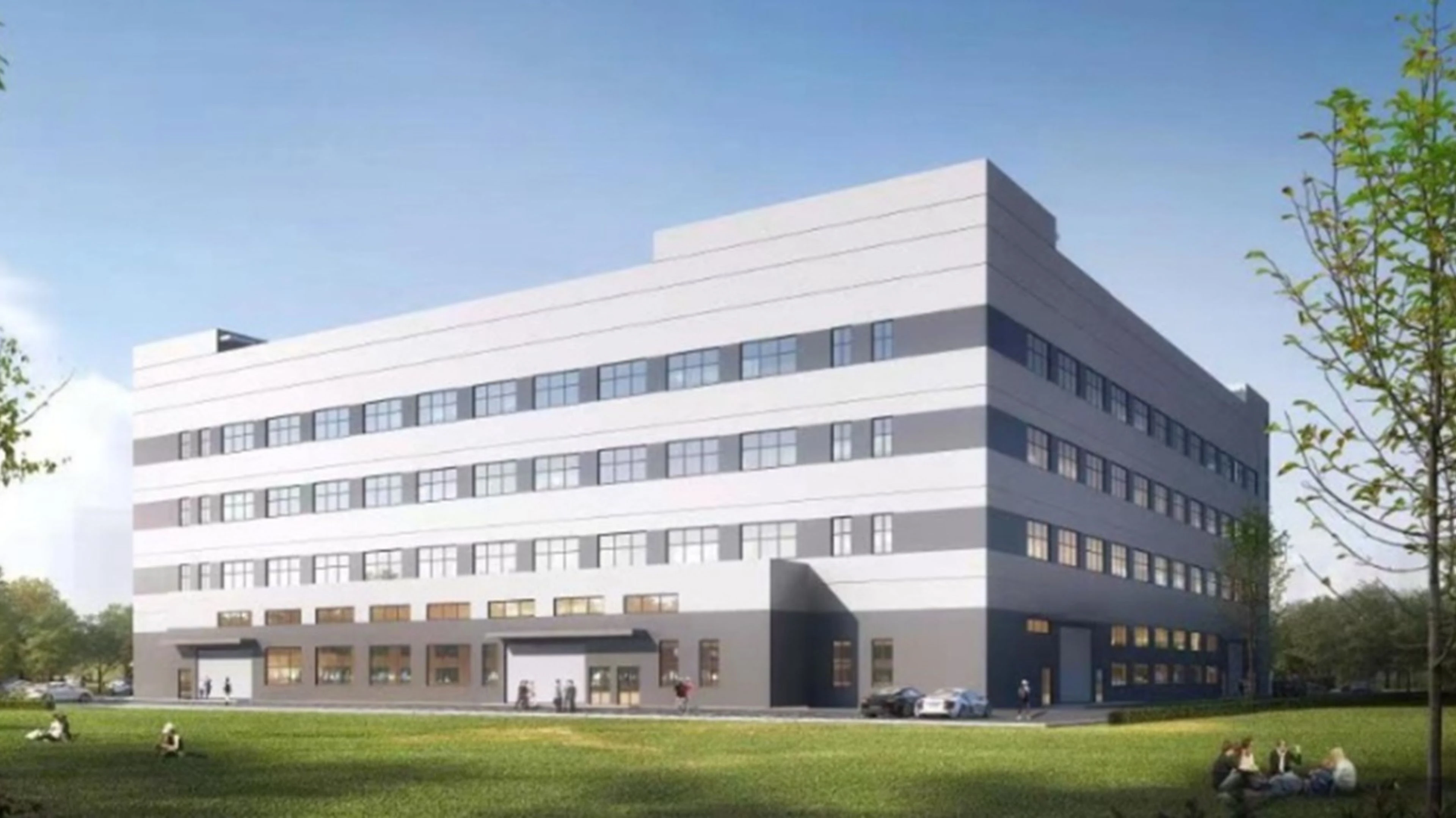 A modern gray and white multi-story building with large windows and Chinese characters on its facade, next to a stone plaque and a separate industrial building labeled BTY under a blue sky with clouds.