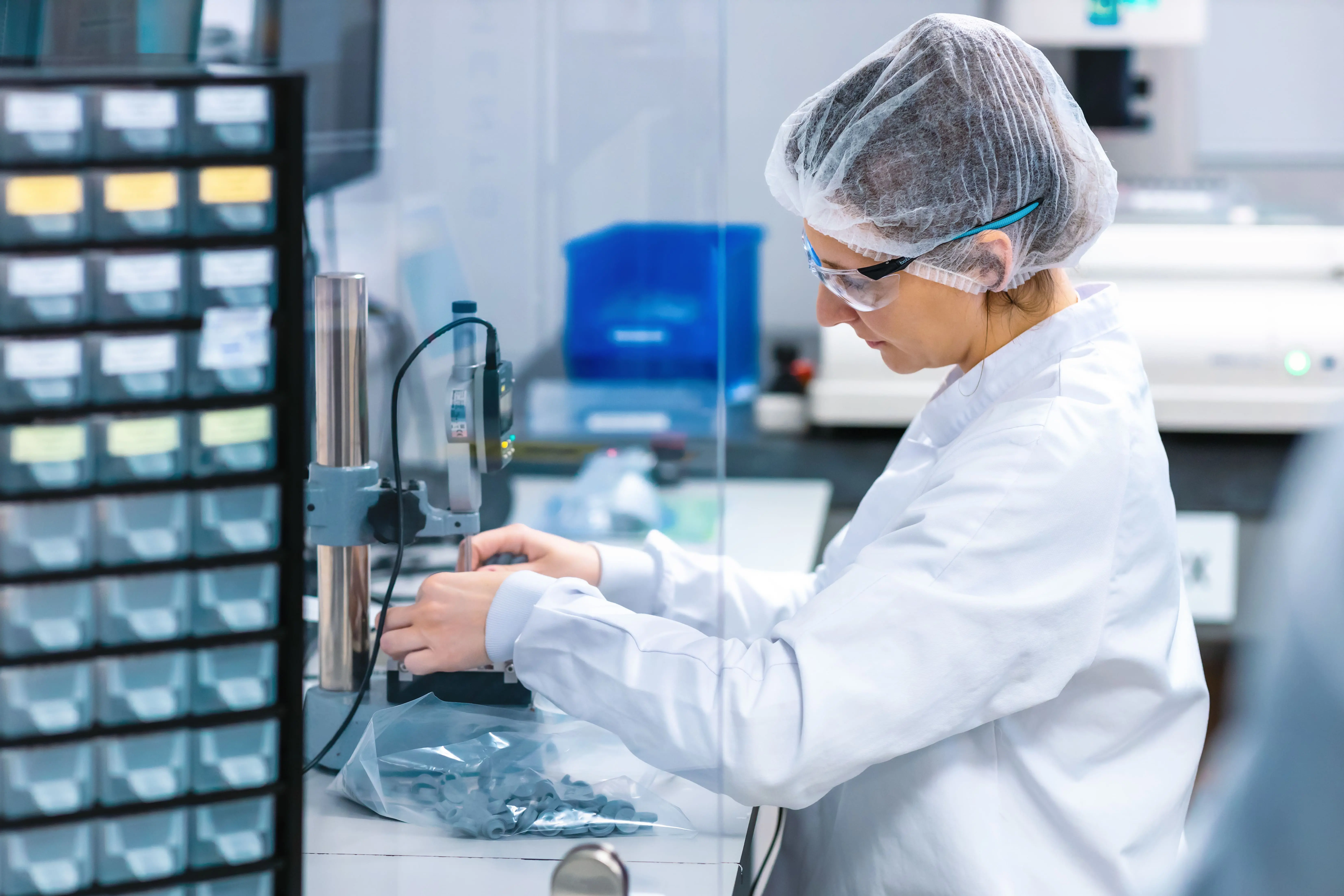 Laboratory operator in cleanroom attire assembling components at a workstation with tools and small parts visible