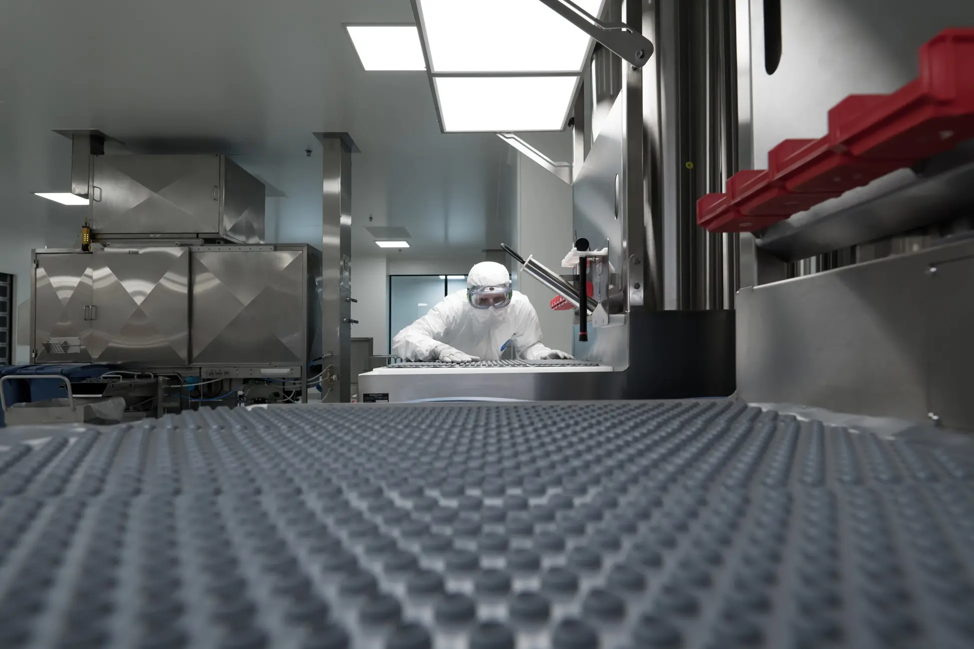 Cleanroom operator in a sterile gown, working on injectable drug primary pacakging components in a controlled manufacturing environment