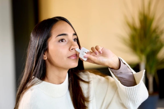 Woman in white jacket administers a single precise dose from an Aptar Unidose liquid nasal spray device zoom view