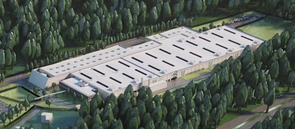 Aptar Oyonnax's large, modern industrial building with a white roof is surrounded by dense green trees and greenery, viewed from above. The rectangular structure features multiple rooftop vents and is accessible by a road.