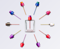 A clear perfume bottle sits at the center, surrounded by twelve colorful plastic fragrance pumps from the Color Code by Aptar collection, arranged in a circular pattern on a light background. Each pump features a distinct color and a long attached diptube