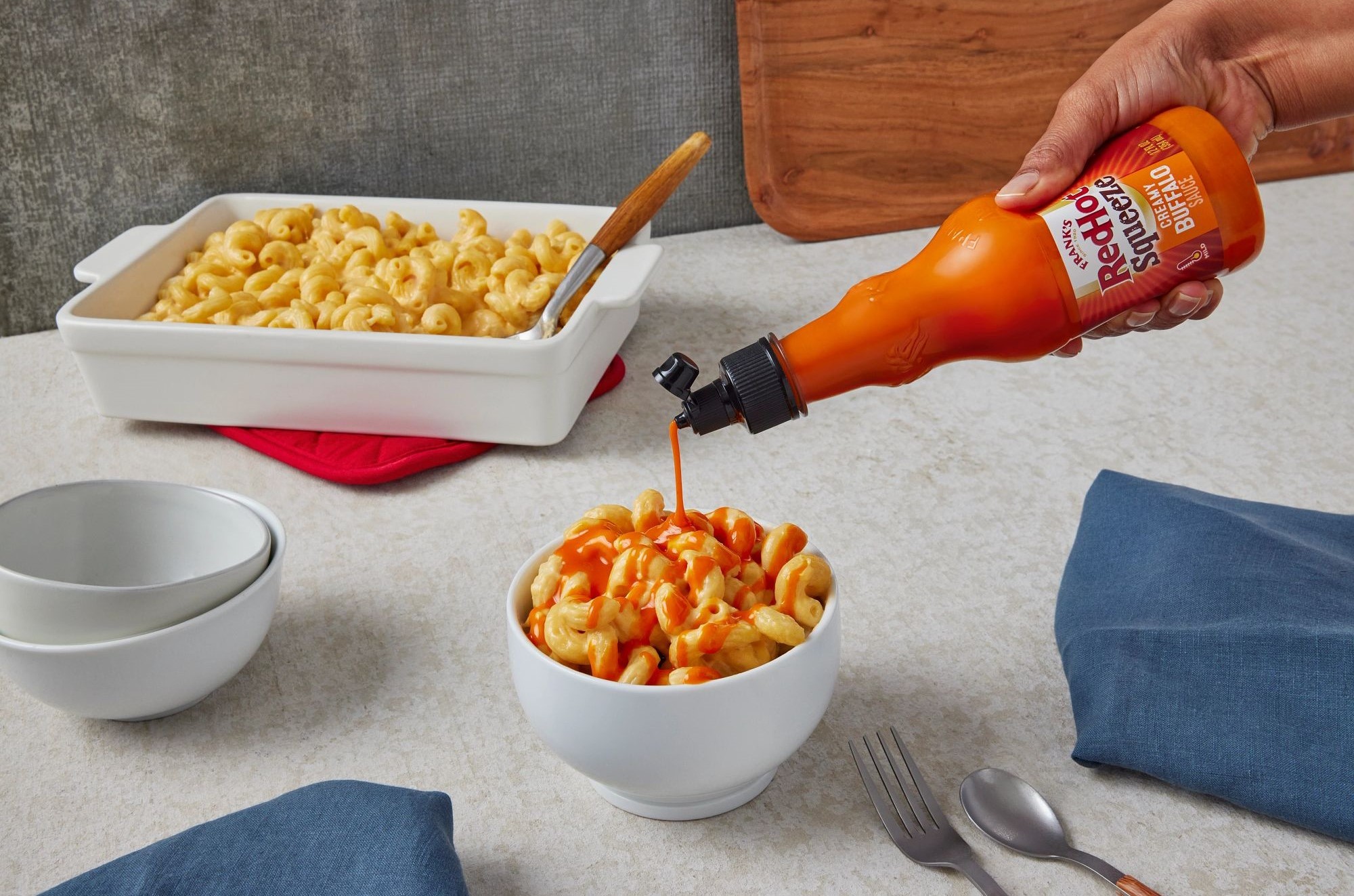A person pouring some hot sauce on a bowl of mac and cheese