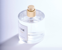 A clear glass perfume bottle with a gold prestige fragrance pump and a white label reading INUNE Pear Eau de Toilette is shown on a white surface with soft lighting and subtle shadows.