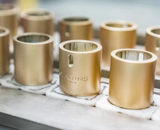 A picture of the Clarins double serum cap with logo on the manufacturing line indicating that a logo is a strong representation of the brand equity of custom primary beauty packaging