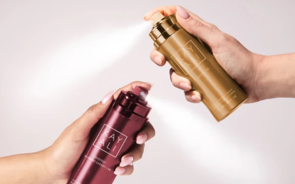 Two premium aerosol All Over Spray in use with hands on actuator dispensing a cloud-like spray