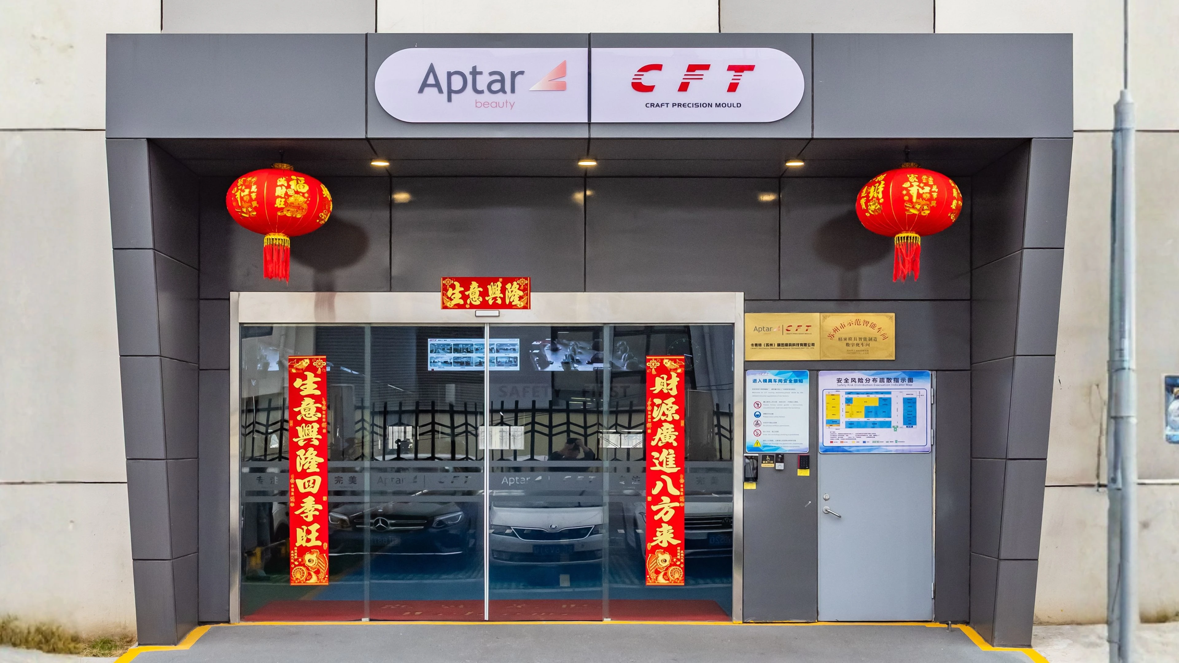 The entrance of BTY's CFT molding manufacturing facility in Suzhou, China. A modern building decorated with red Chinese lanterns and banners, featuring the logos Aptar Beauty and CFT above the glass doors. Inside, several cars are visible through the glass.